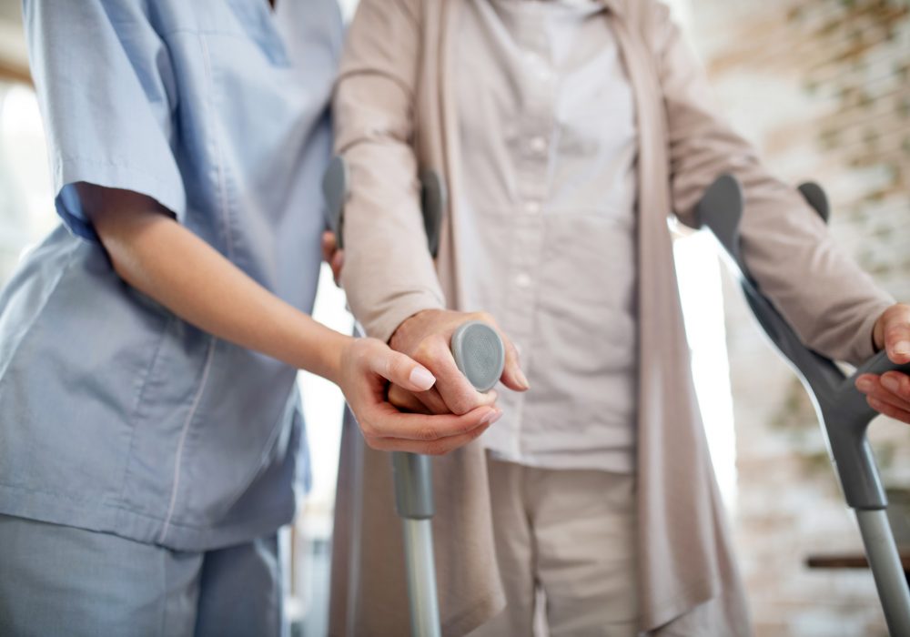Nurse wearing uniform supporting woman with crutches Nurse support. Young but professional nurse wearing uniform supporting woman with crutches